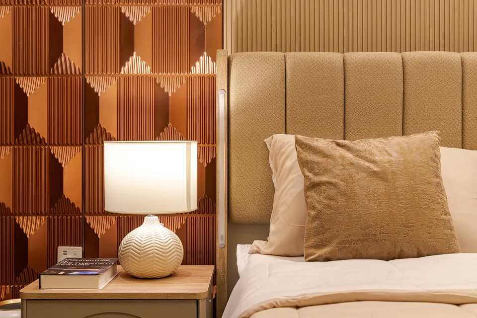 Imperial Avenue Apartment, Downtown Dubai: white ceramic lamp by a beige channelled headboard and copper-toned wall panel.