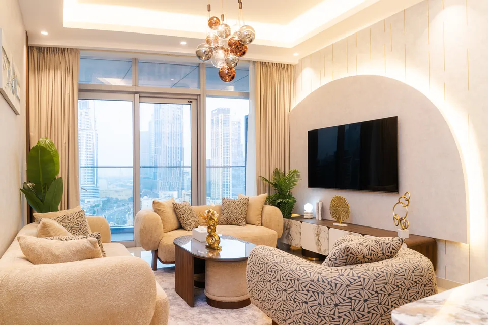 Imperial Avenue Apartment، وسط مدينة دبي: غرفة معيشة بقوس مضاء خلف التلفاز، وأرائك بلون كريمي، وإطلالات على المدينة.