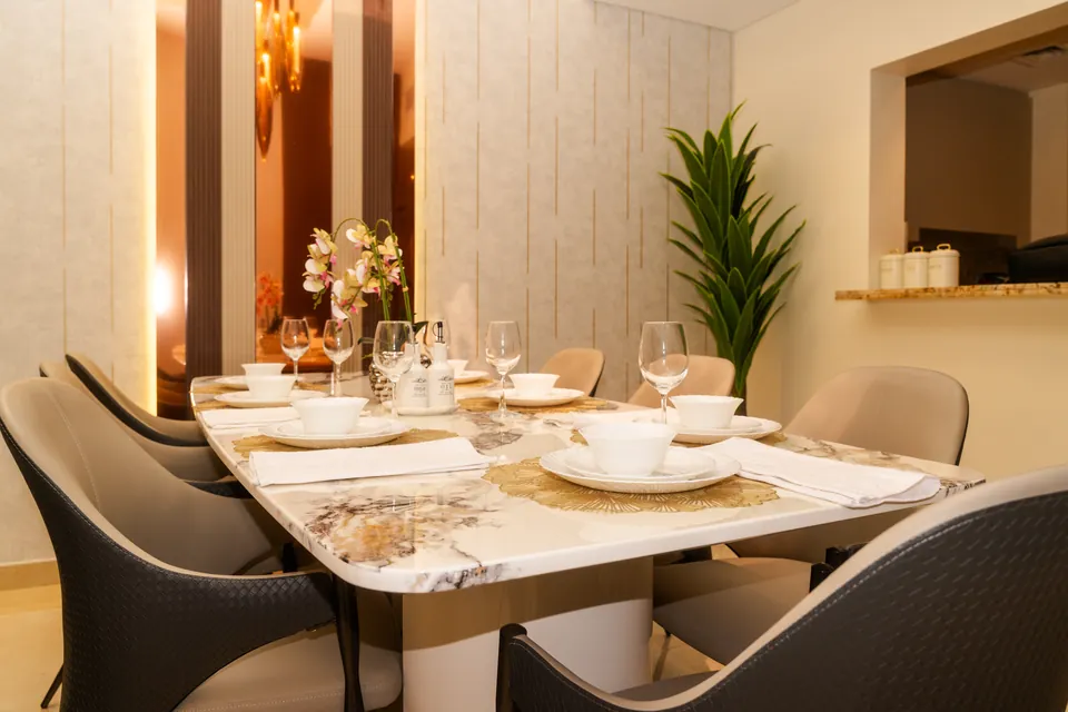 Imperial Avenue Apartment, Downtown Dubai: dining table laid with grey chairs, orchids and a copper-toned mirror panel.
