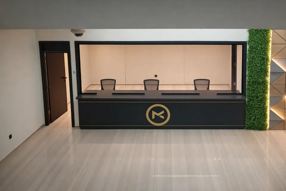 MK Pay,里加区:玻璃后方的服务柜台配有三把座椅,另有金色圆形标志和绿植墙。