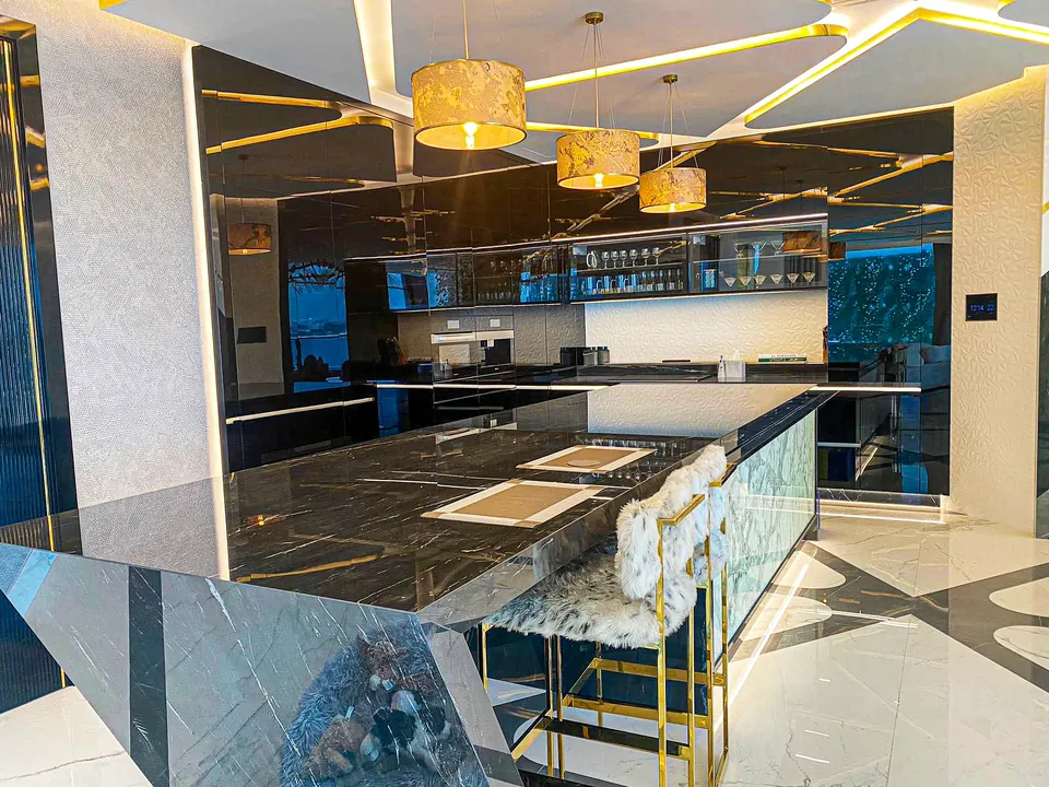MK Villa, Palm Jumeirah: kitchen with a black marble-look island, gold drum pendants and a fluffy white bar stool.