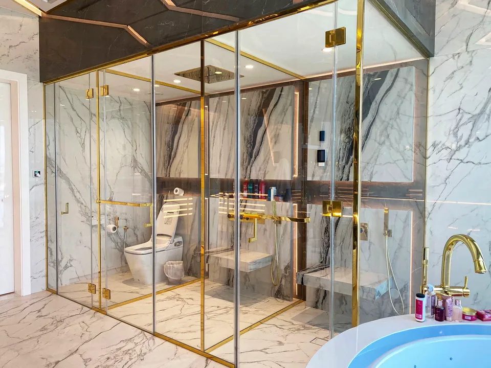 MK Villa, Palm Jumeirah: marble-look bathroom with a gold-framed glass shower, gold tap and a round bath.